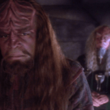 worf in his religious attire is in the foreground looking conflicted as a priest in the background looks on